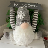 Decorative gnome with striped socks and a 'WELCOME' sign on a white surface.