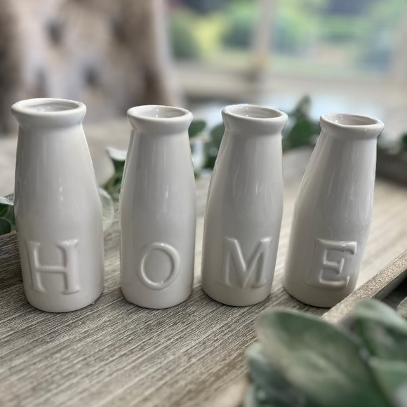 Four white ceramic vases on a table with 'HOME' embossed on them.