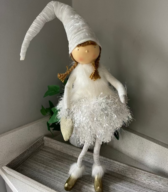White fairy doll with long hair on a wooden surface against a neutral wall